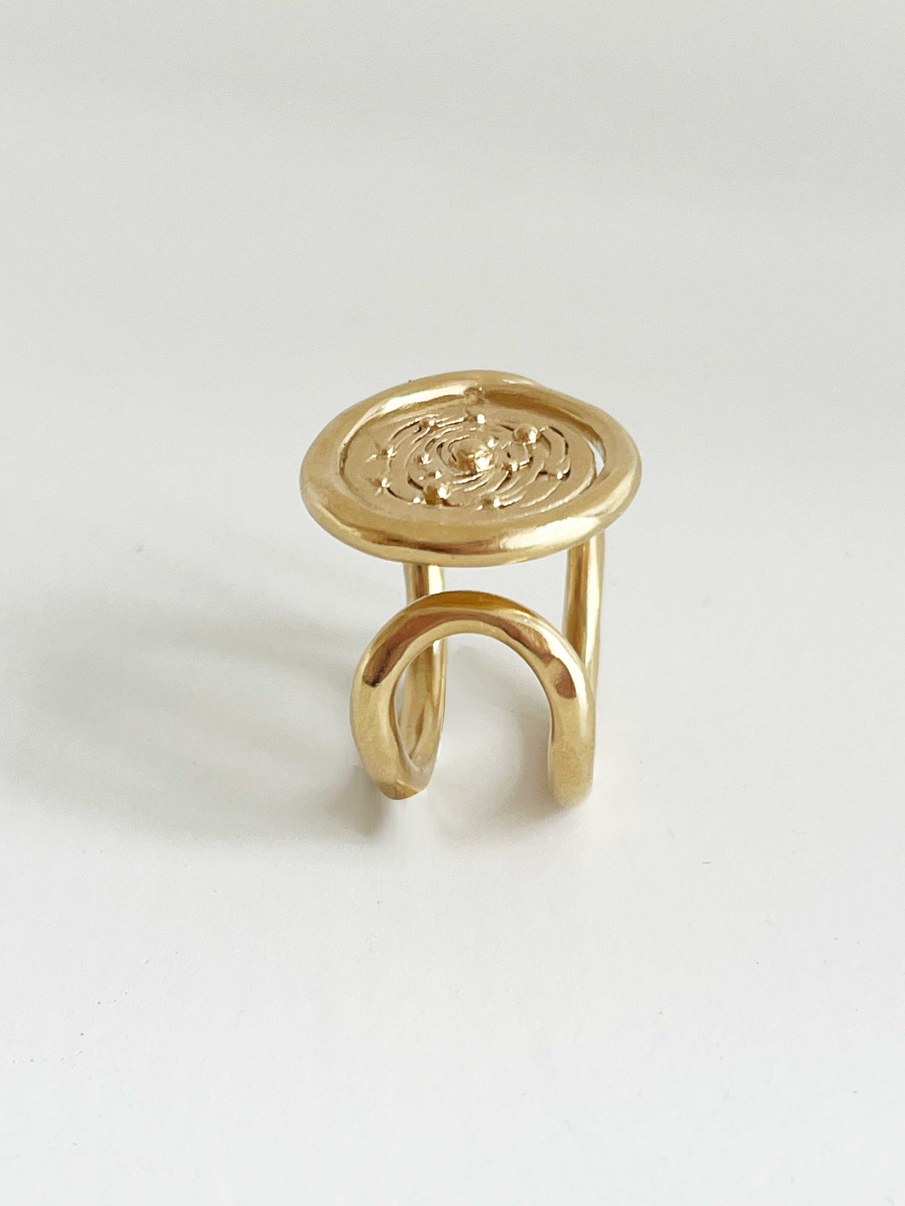 une bague chevaliere avec un plateau en bas relief orné d'une galaxie, vue de coté, gauche