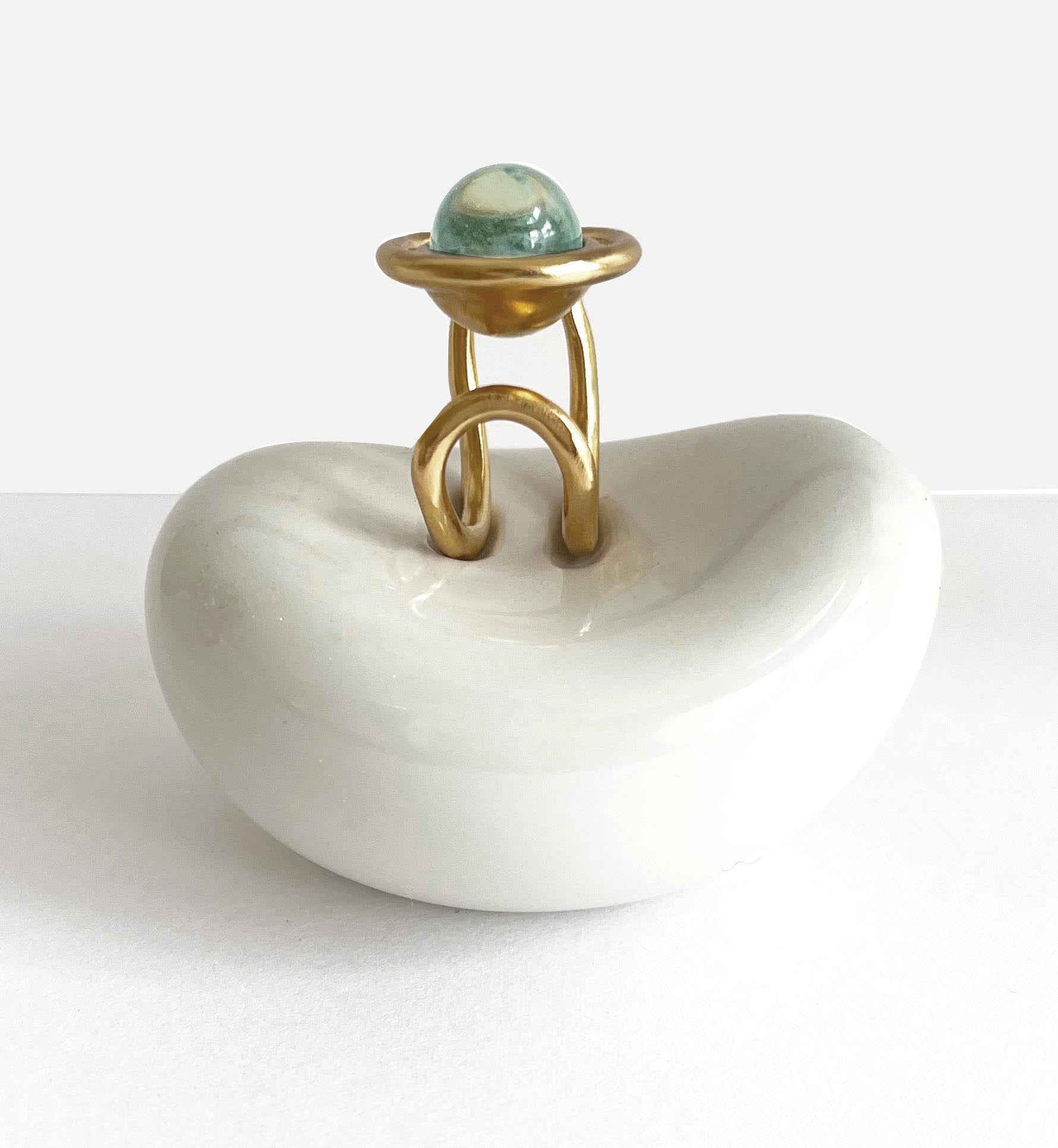 une chevalière eclipse en vermeil sur son presentoir en forme de haricot, vu de face profil ou l'on voit l'anneau entourant la perle de verre de murano et la coupelle surlaquelle est poséee la perle